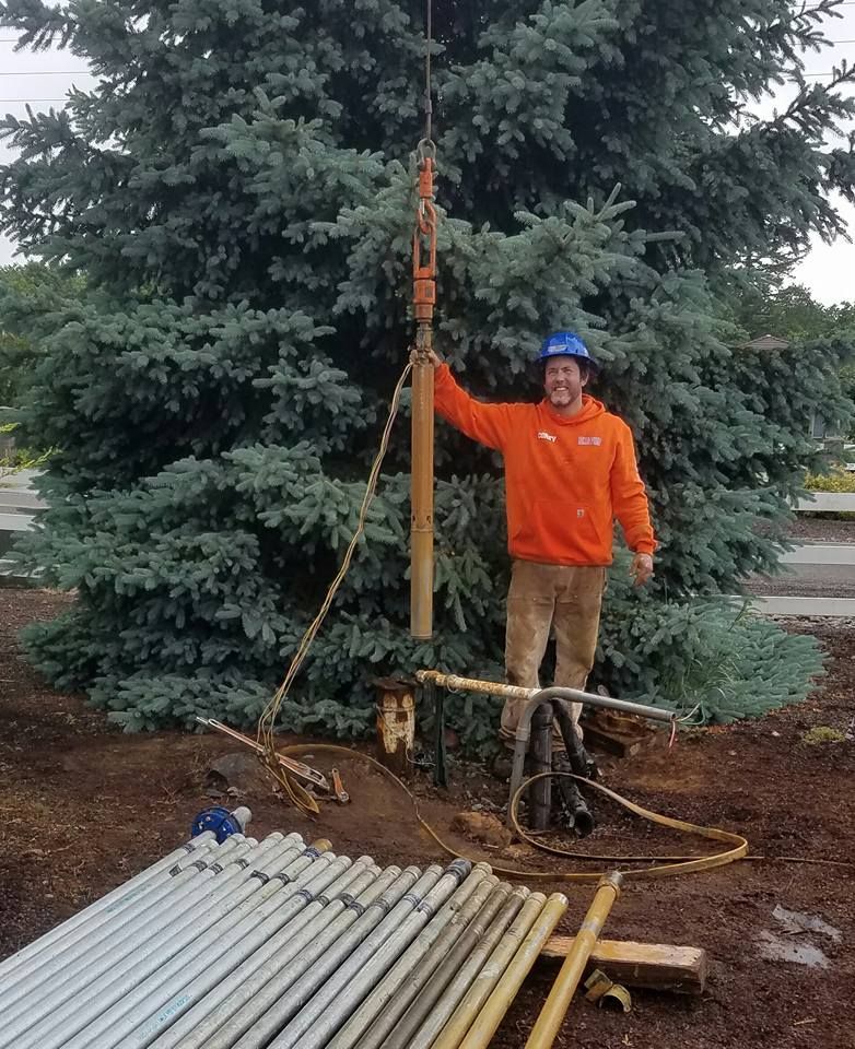 Man in orange jacket standing near drilling equipment by a tree. Man in orange jacket standing near drilling equipment by a tree.
