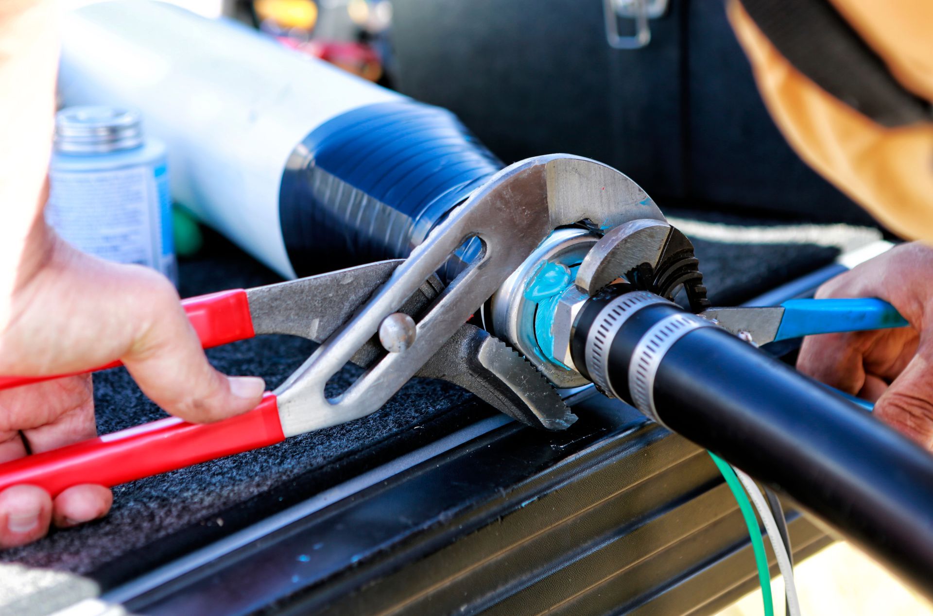 Hands using pliers and wrench to connect a black hose to a white pipe. A blue gasket is visible. Hands using pliers and wrench to connect a black hose to a white pipe. A blue gasket is visible.