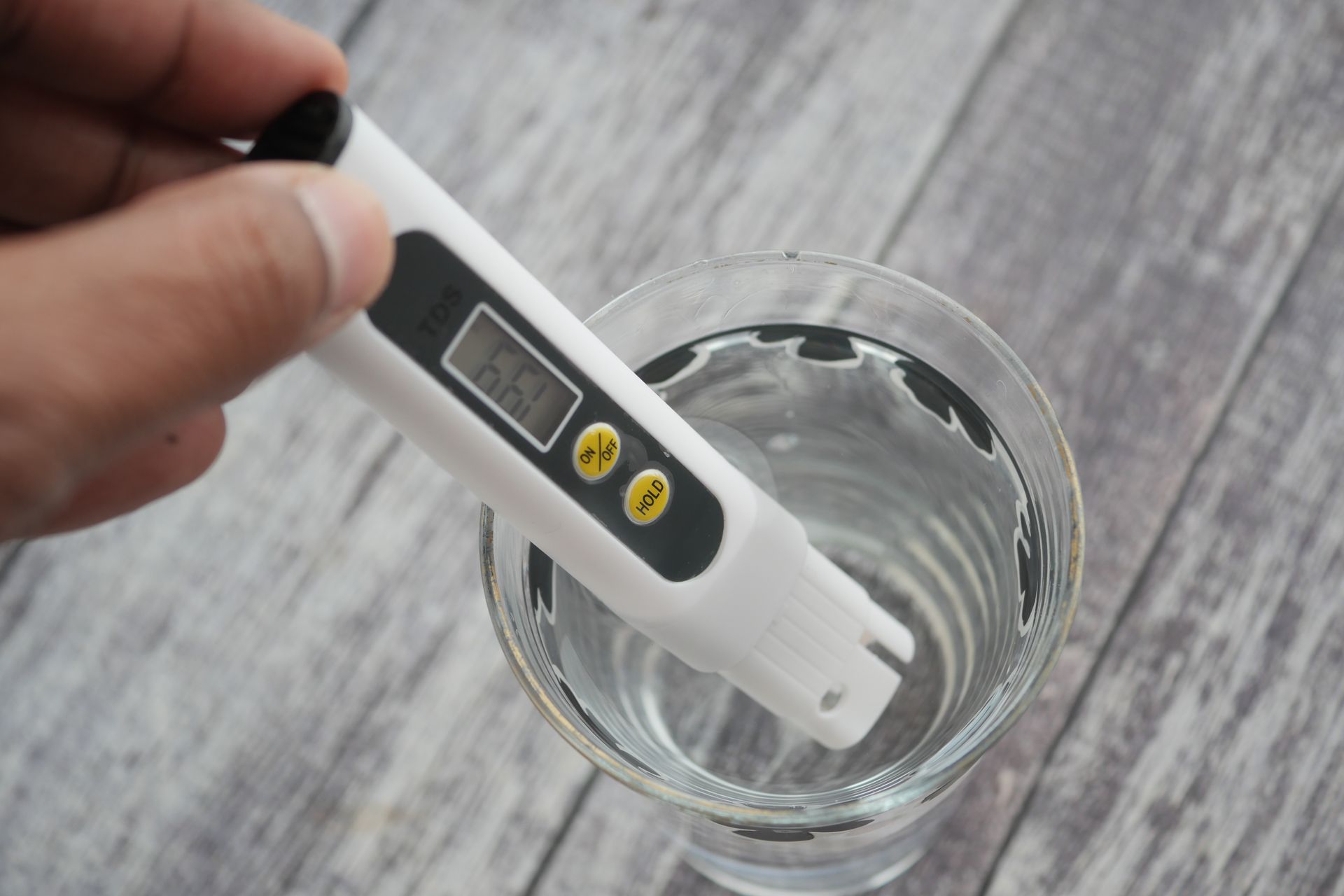 Hand holding a water quality tester in a glass of water on a wooden surface. Hand holding a water quality tester in a glass of water on a wooden surface.
