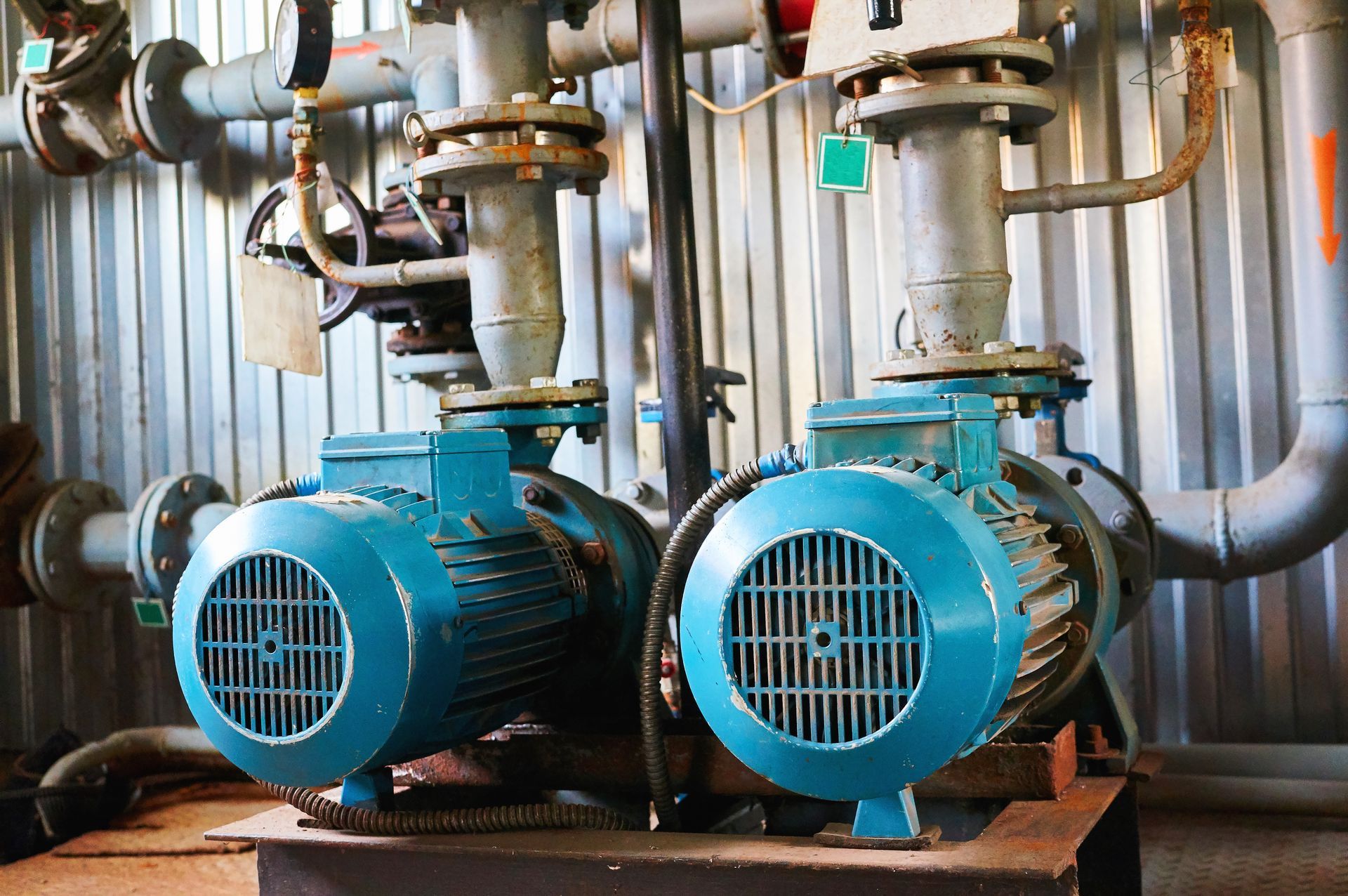 Two blue industrial pumps connected to pipes, in a room with corrugated metal walls. Two blue industrial pumps connected to pipes, in a room with corrugated metal walls.