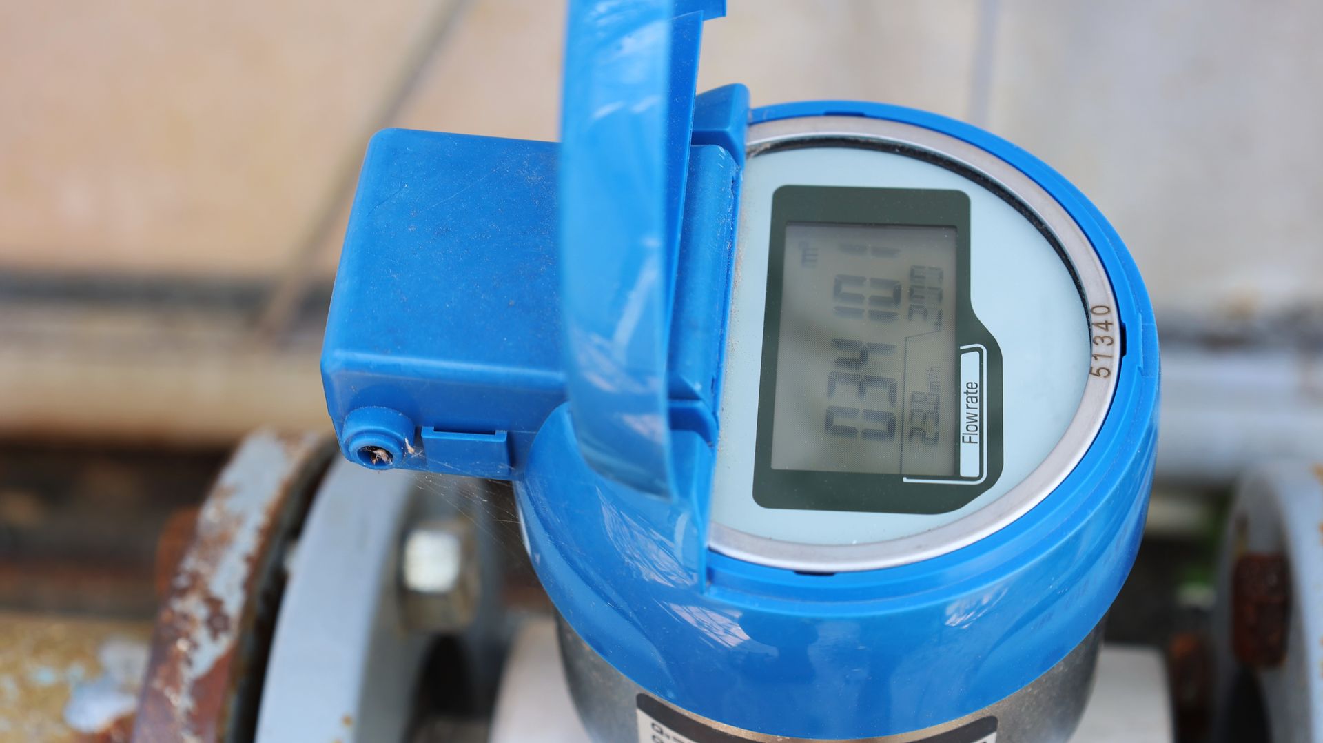 Blue flow meter display with readings, mounted on a pipe. The cover is open.