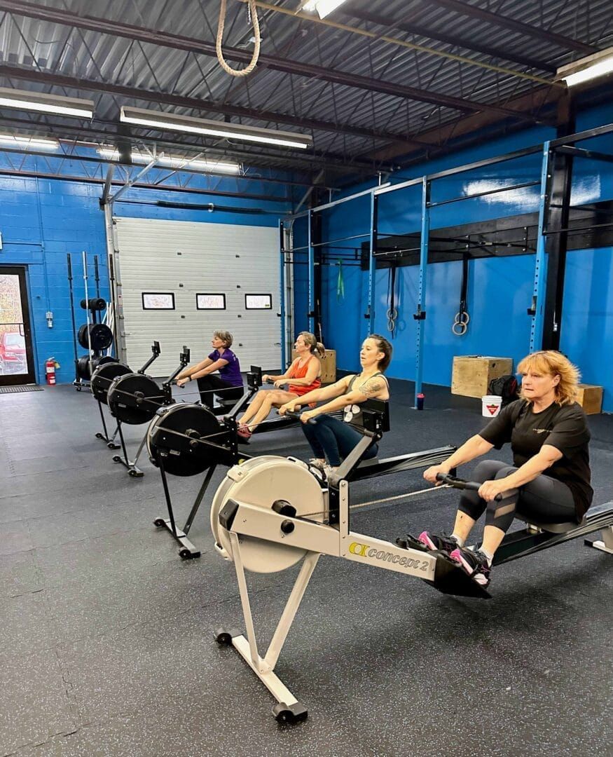 A group of people are riding rowing machines in a gym.