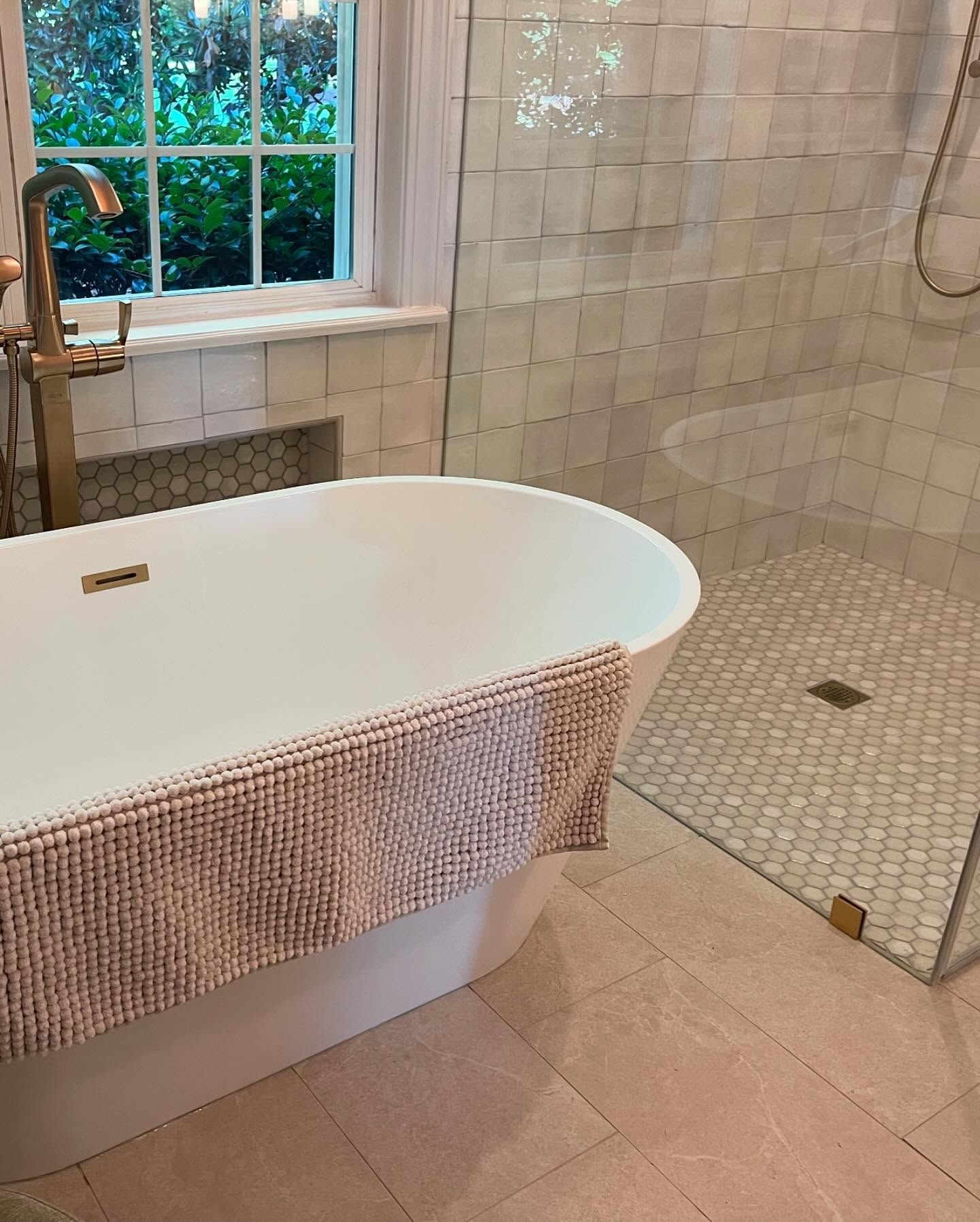 Bathroom with freestanding white tub, glass shower, and gold fixtures. Soft pink bath mat.