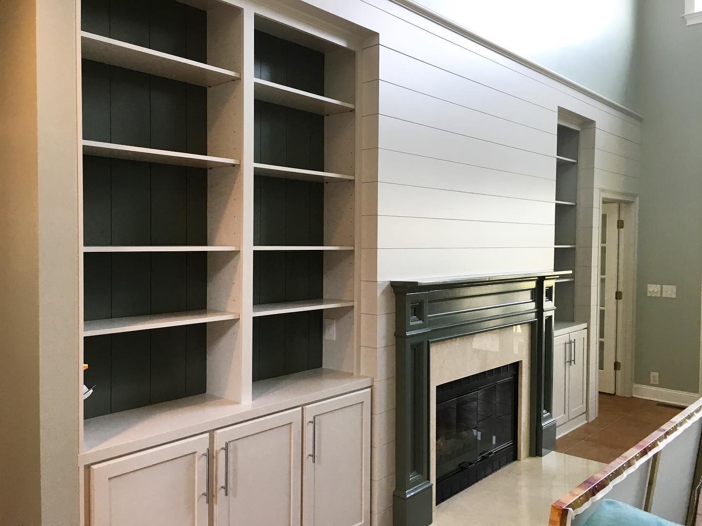 Built-in bookshelves flank a fireplace. The shelves are white with green backs. The fireplace has a dark green mantel.
