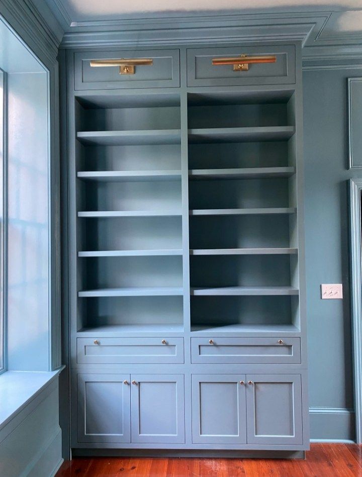 Built-in blue bookshelf with drawers and cabinets, brass hardware, and empty shelves.