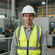 Trabajador con casco blanco y chaleco de seguridad de alta visibilidad en el interior de una fábrica industrial.