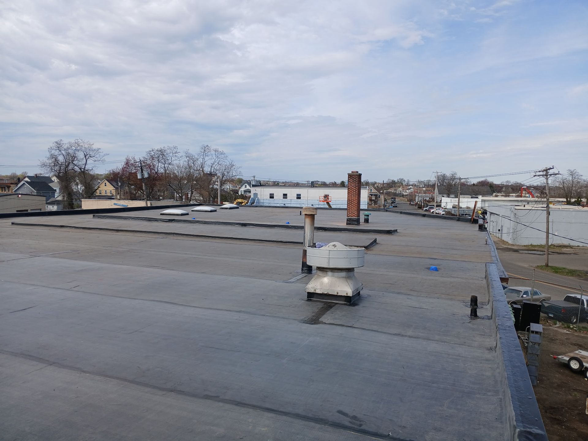 A man is rolling a roll of asphalt on a roof.