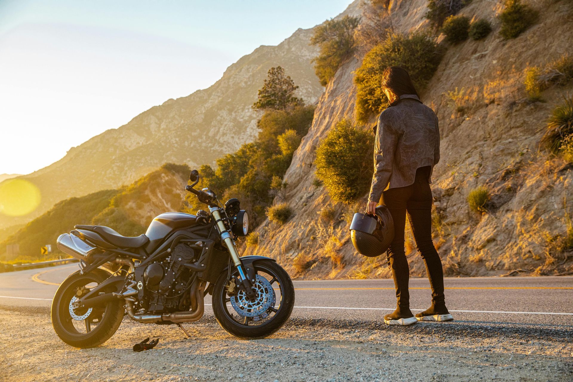 Motorcyclist with helmet beside a bike on a mountain road—motorcycle accident lawyer.