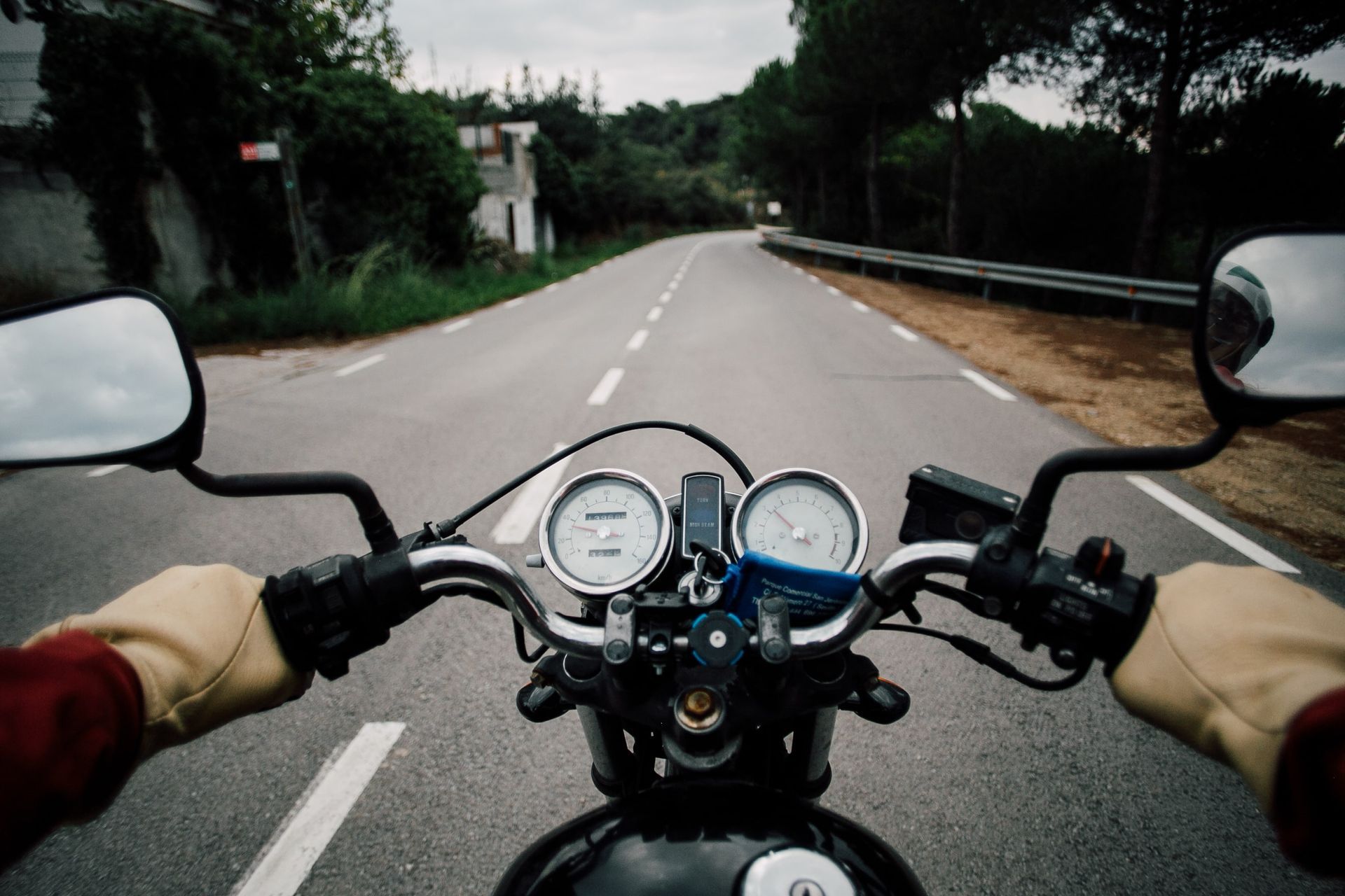 A first-person view from a motorcycle handlebars, showing a paved road winding through a wooded landscape.