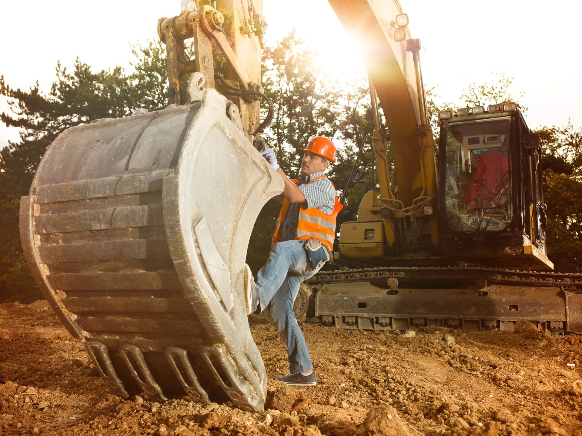 A construction worker is climbing into the bucket of an excavator.