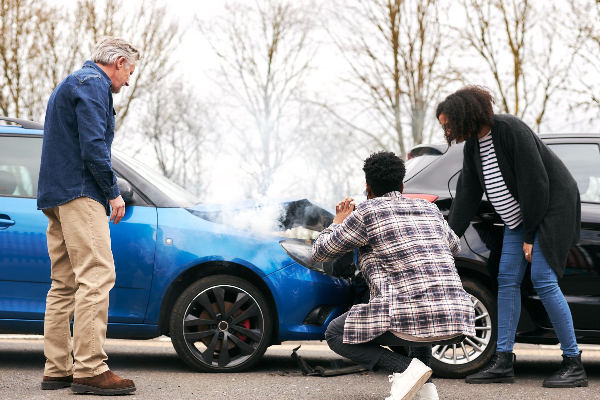 A group of people are standing around a car that has been involved in a car accident.