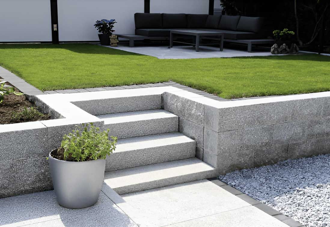 Modern concrete steps to a raised lawn, with a potted plant and black outdoor sofa in a patio area