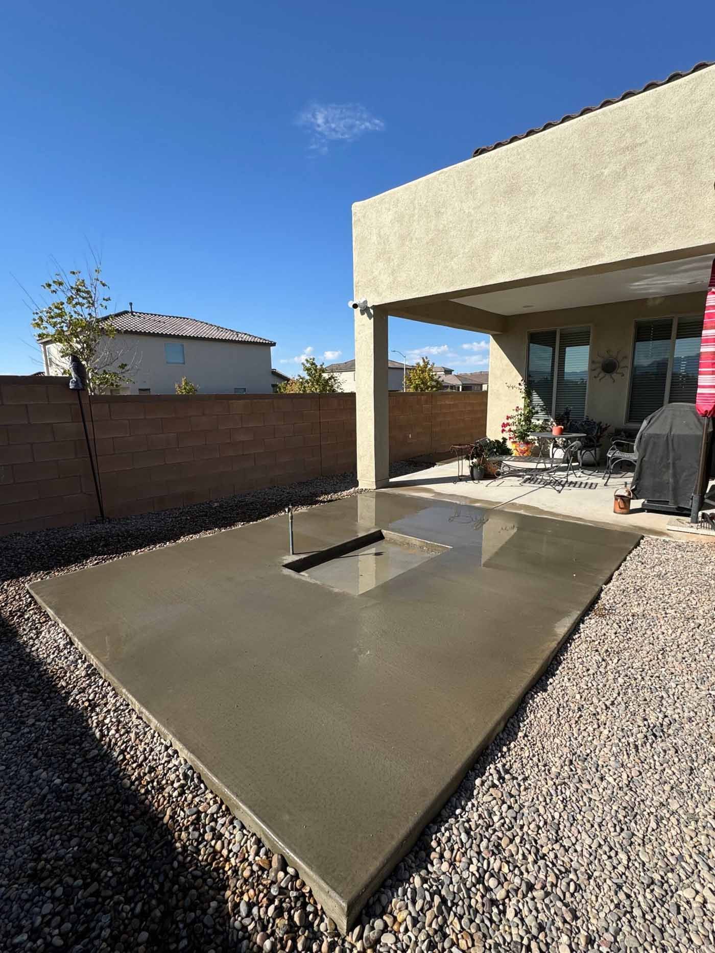 Backyard concrete patio with a covered pergola and gravel landscaping under a clear blue sky