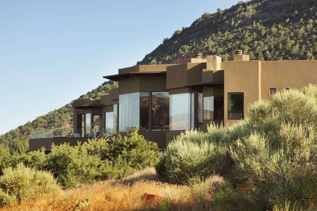 Modern desert house with large windows nestled among shrubs near a rocky hillside