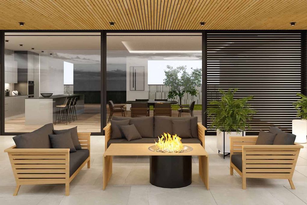 Modern patio with wooden lounge chairs, dark cushions, and a central fire table in front of glass doors.