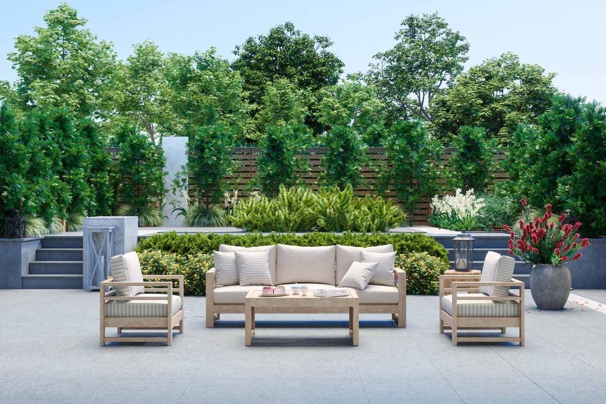 Modern patio with beige sofa, matching chairs, low table, and potted plants against a lush green hedge.
