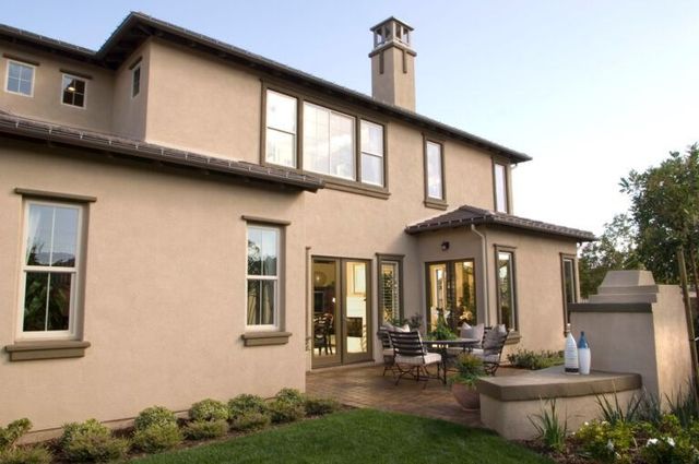 Two-story beige house with patio seating and a small lawn in the backyard