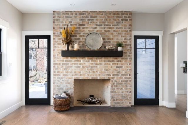 Bright living room fireplace with exposed brick, black mantle, and glass doors on both sides