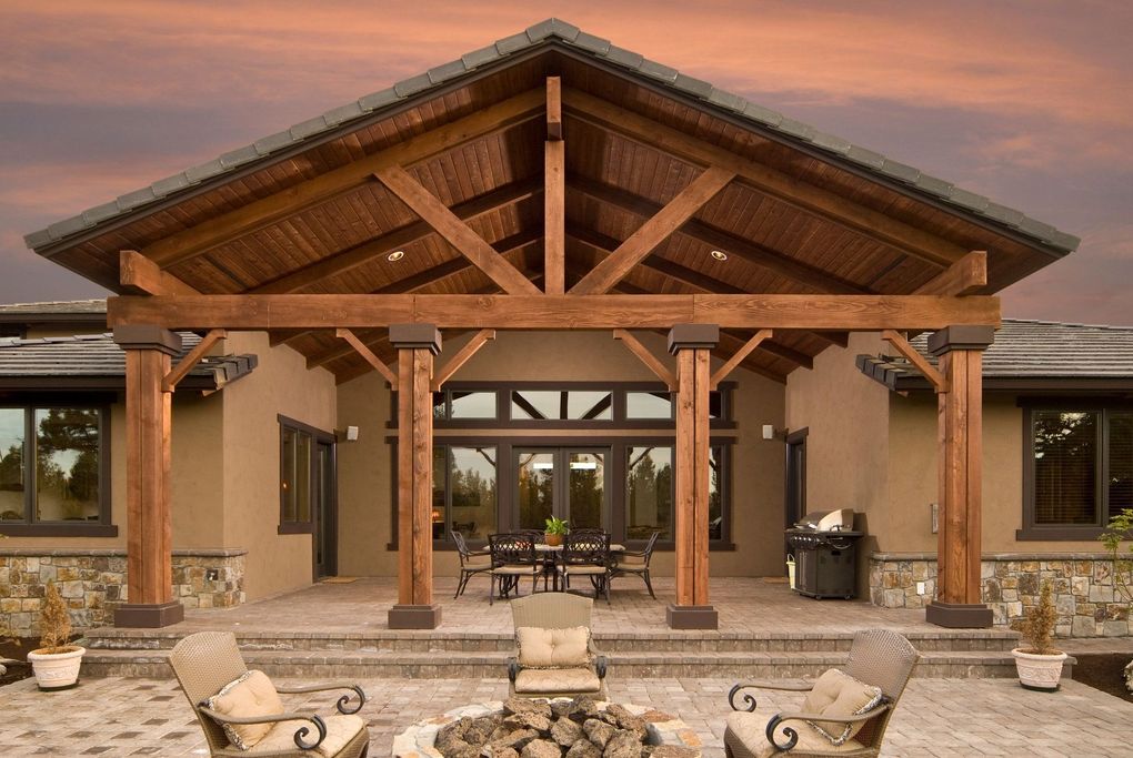 Rustic porch with exposed wood beams, stone columns, and seating at sunset