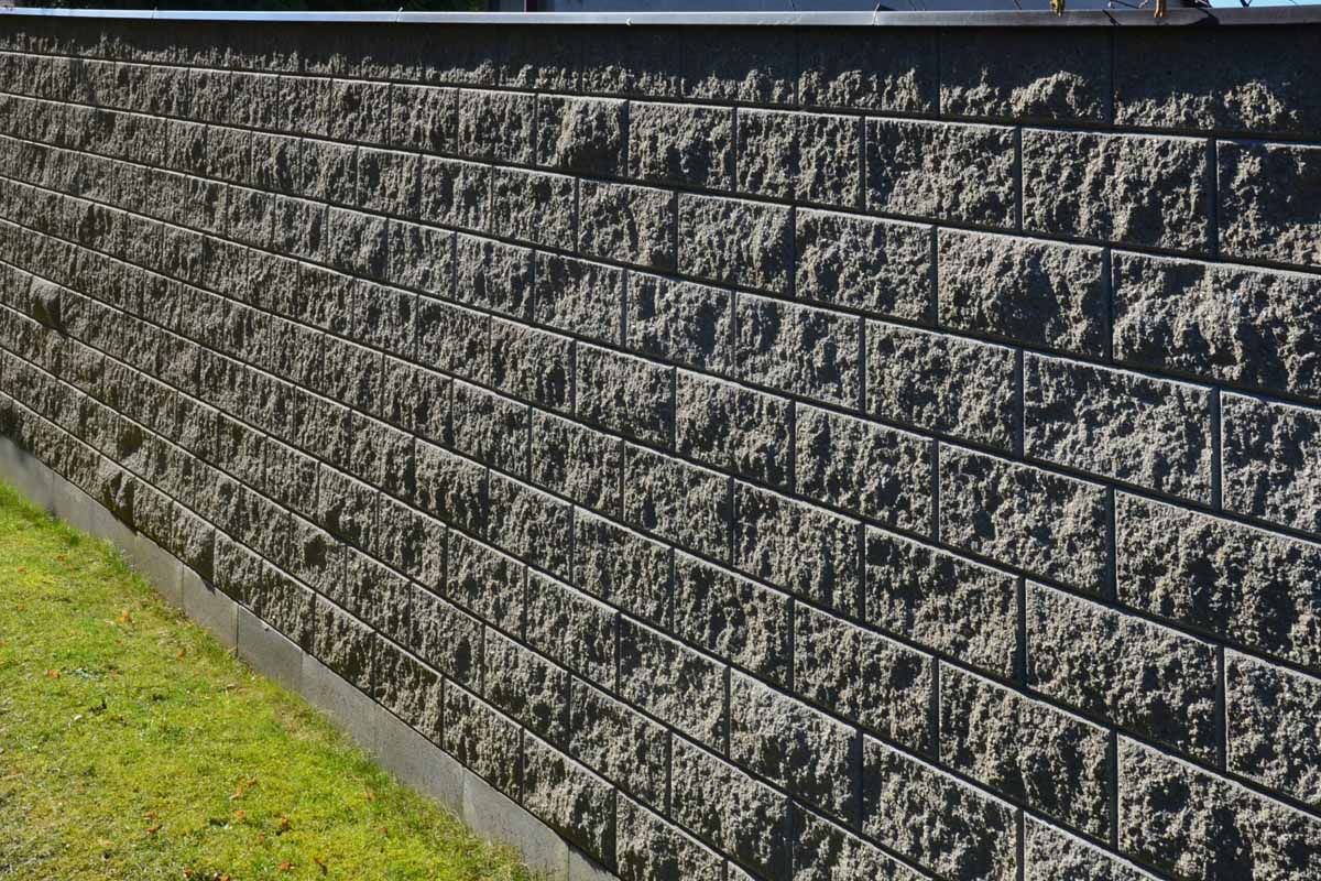 Gray cinder block retaining wall beside a strip of green grass in sunlight