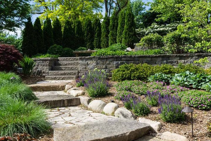 Stone garden steps leading to tiered retaining walls, with lush green shrubs and purple flowers.