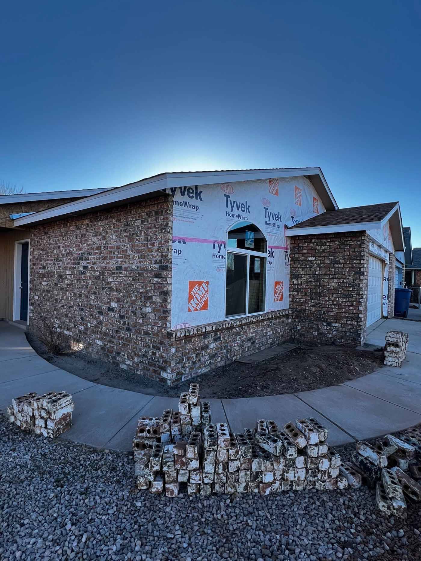 Single-story brick house under construction with exposed insulation and stacked cinder blocks in front.