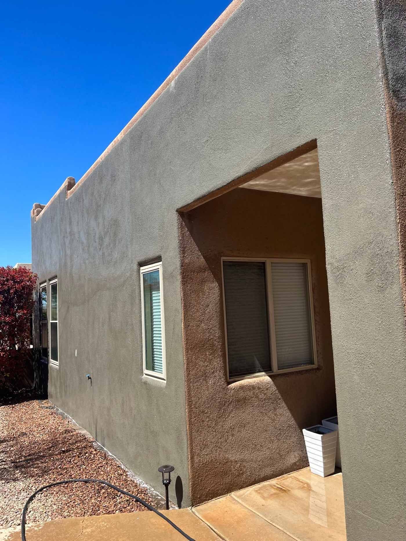 Stucco house exterior with a covered entry, windows, and a blue sky overhead