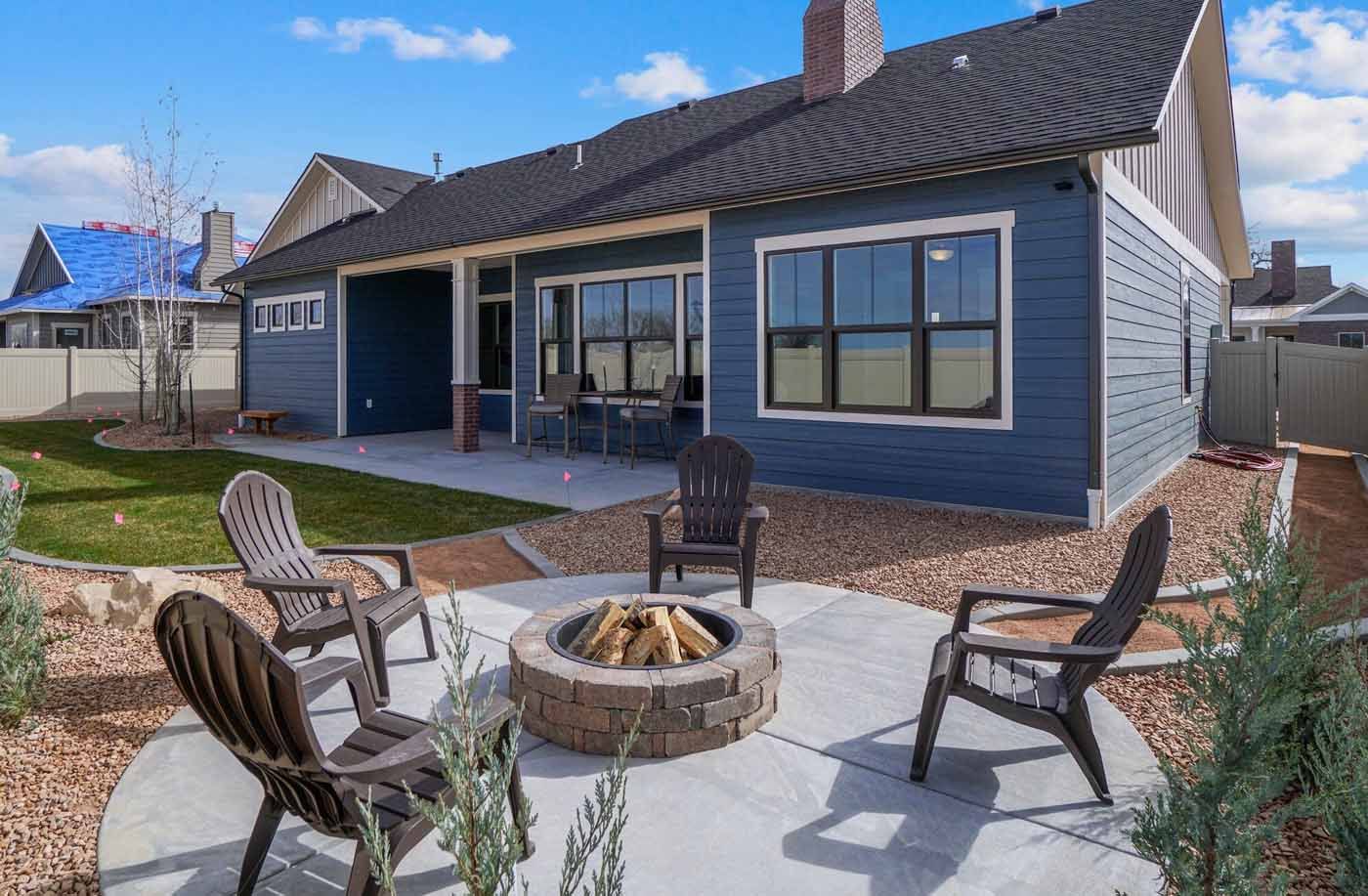 Backyard patio with fire pit and four chairs beside a blue house under a sunny sky