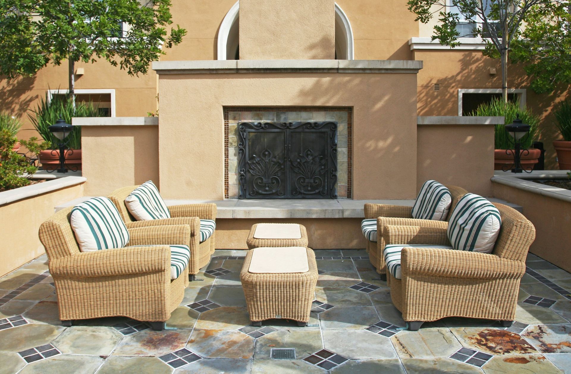 Patio seating area with wicker chairs and ottoman facing an outdoor fireplace on a stone patio