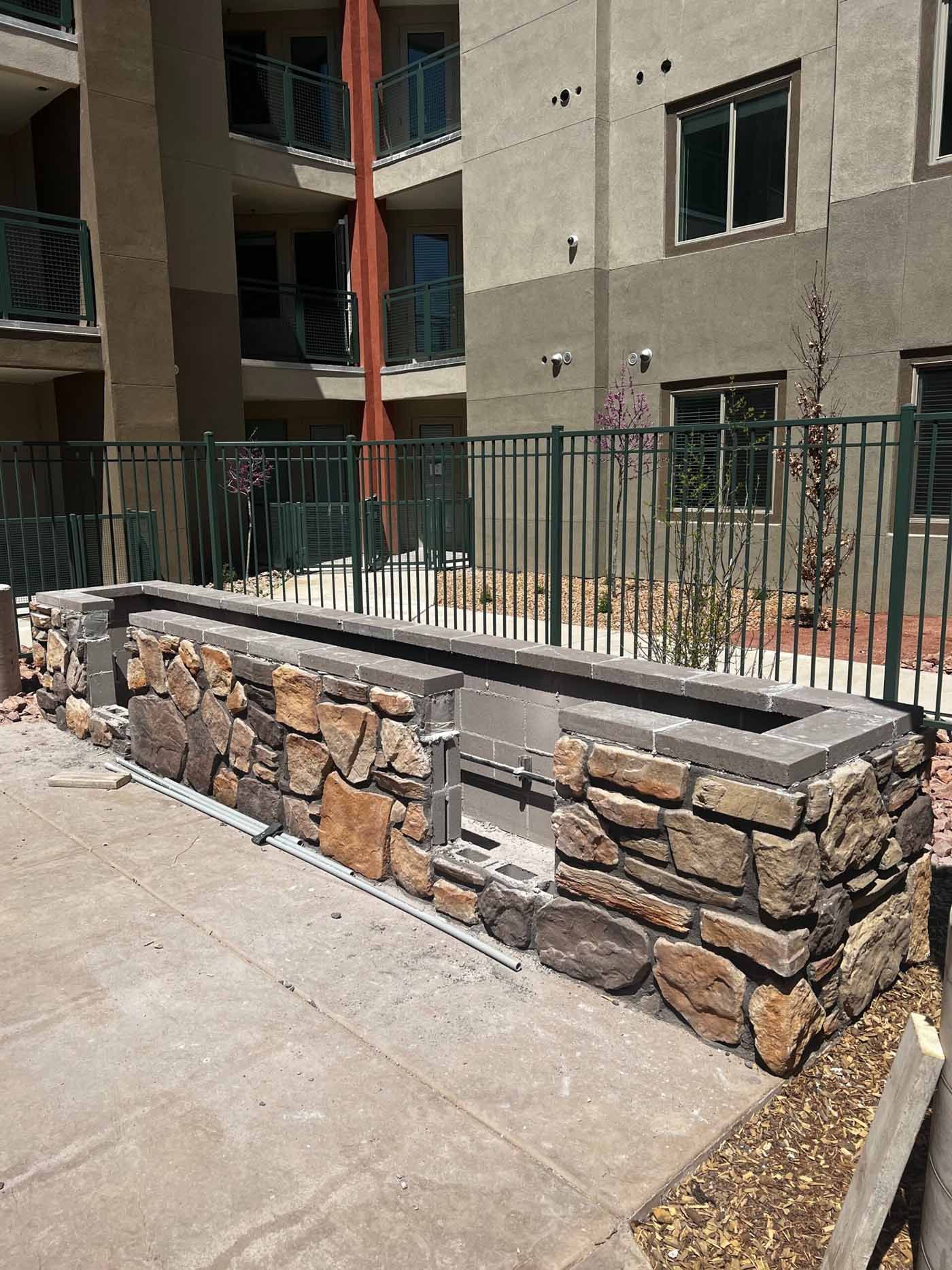Stone retaining wall and metal railing beside a concrete walkway outside an apartment building.