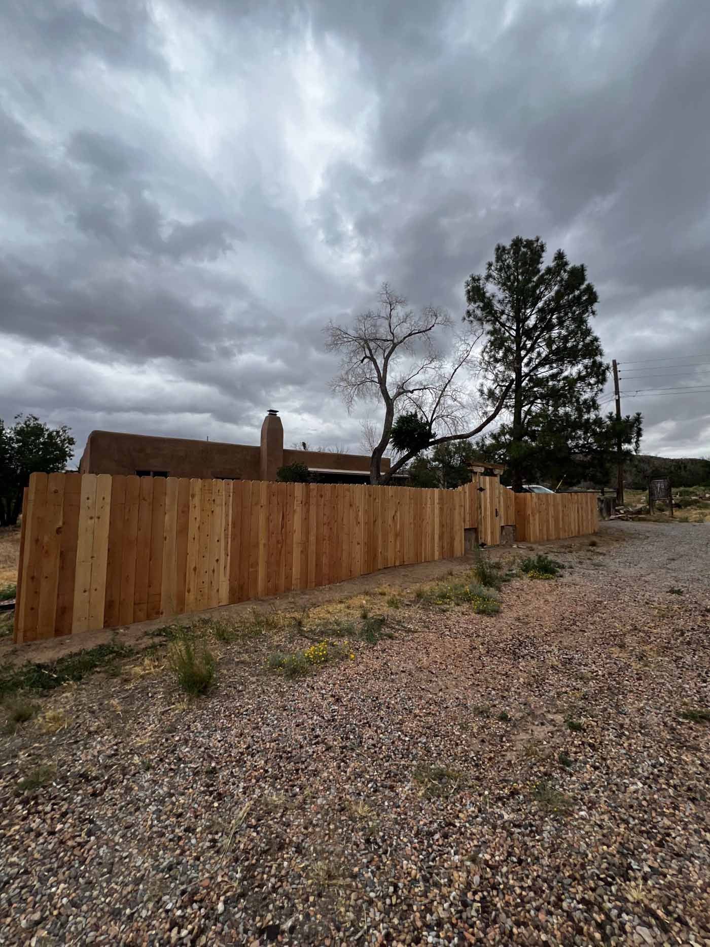 Wooden fence along a gravel road under a dark, stormy sky with trees in the background