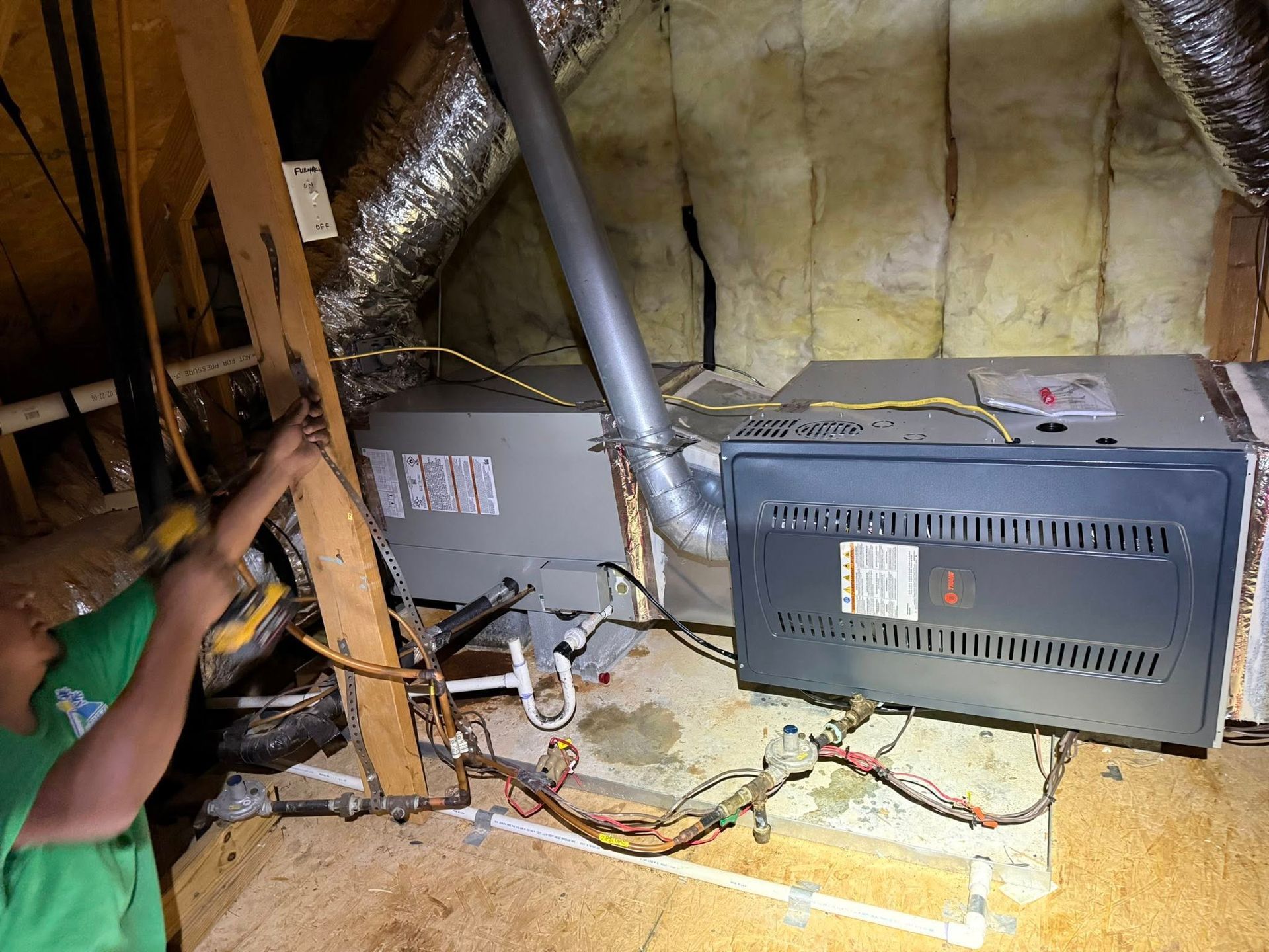 Attic HVAC units with silver ductwork and exposed wiring under a sloped roof.