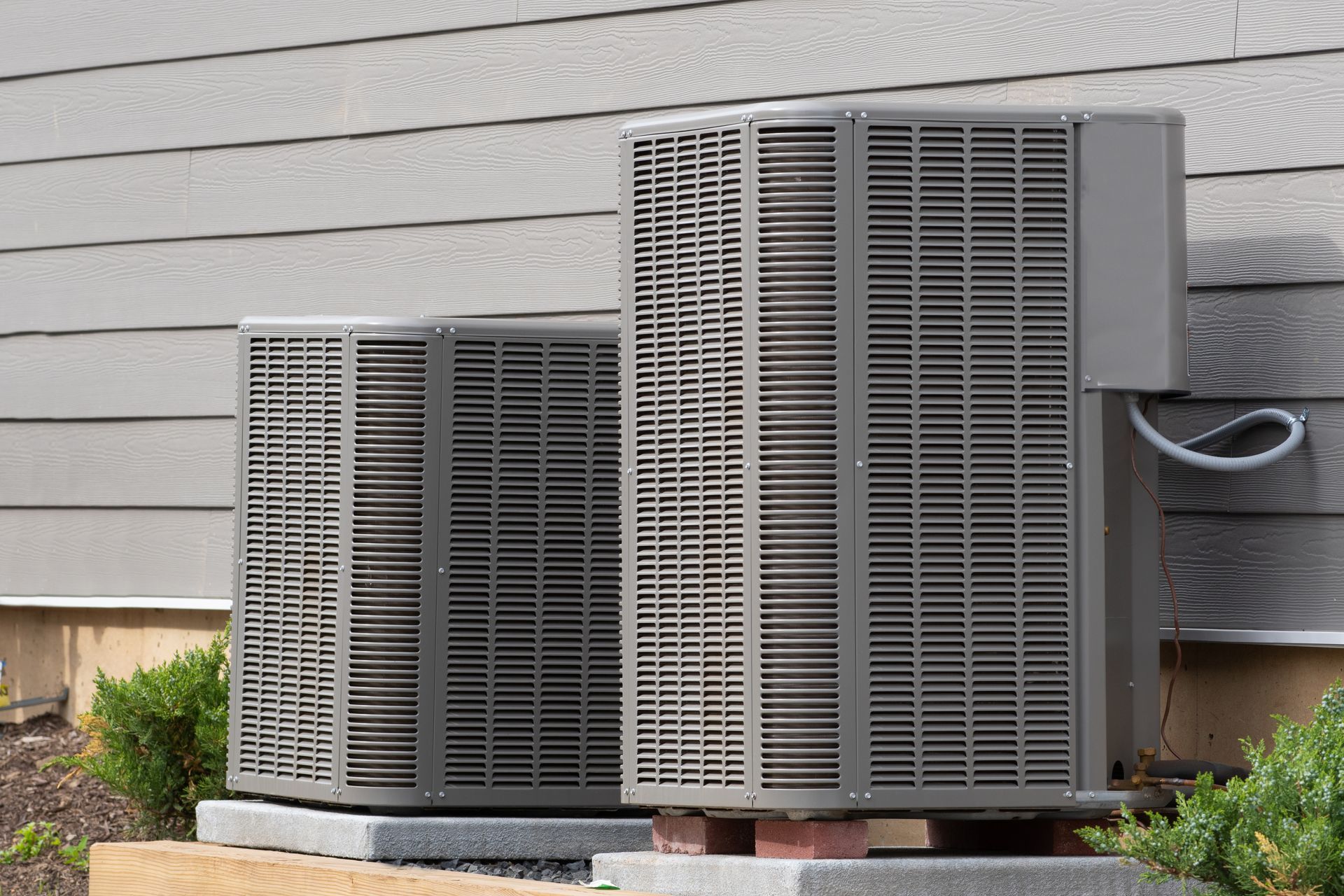 Two outdoor HVAC units beside a house wall on a concrete pad
