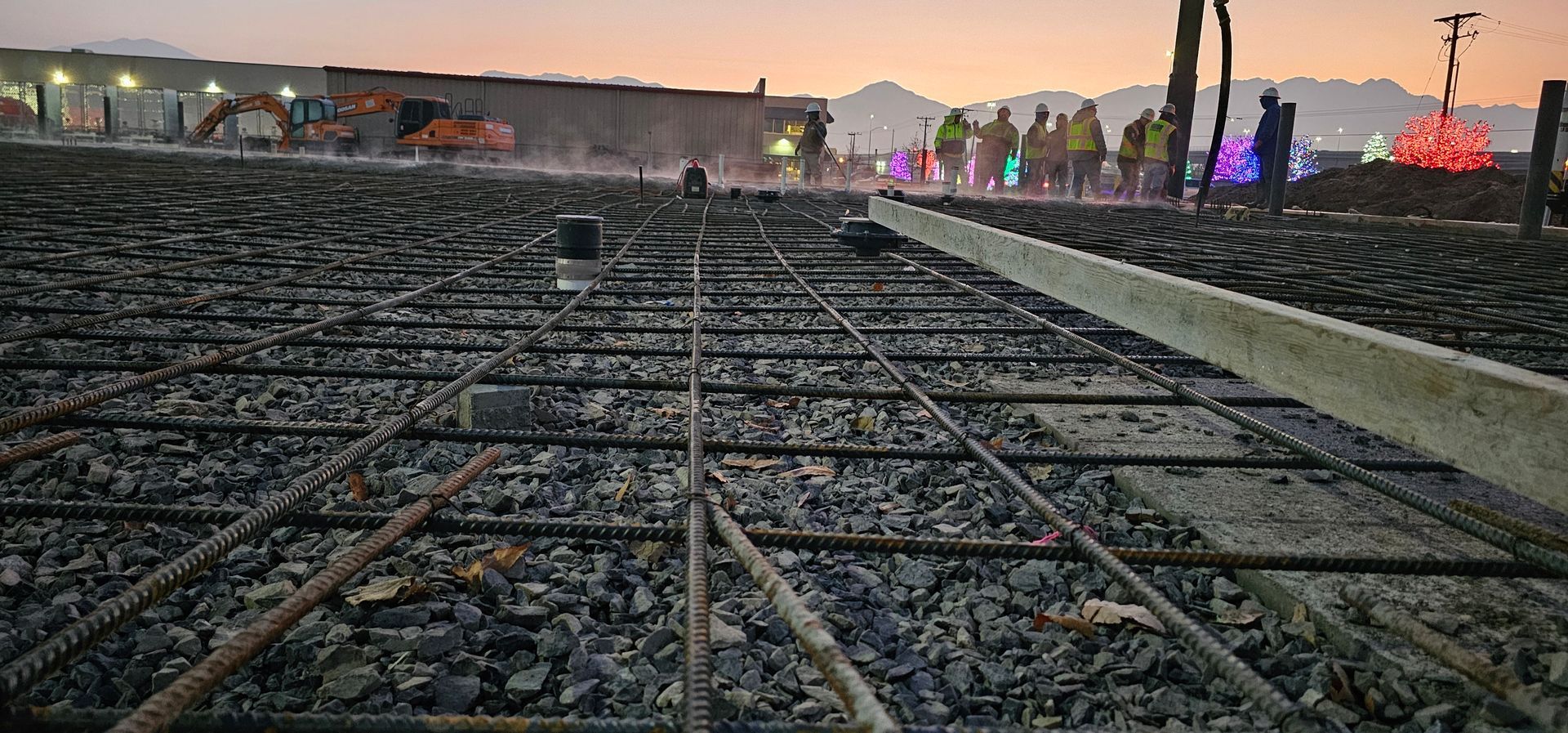 A concrete pump is being used to pour concrete on a construction site with mountains in the background.