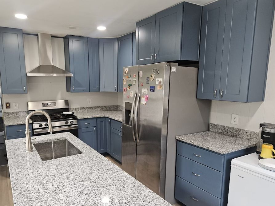 Kitchen with blue cabinets, granite countertops, a center island with a sink, and stainless steel appliances.