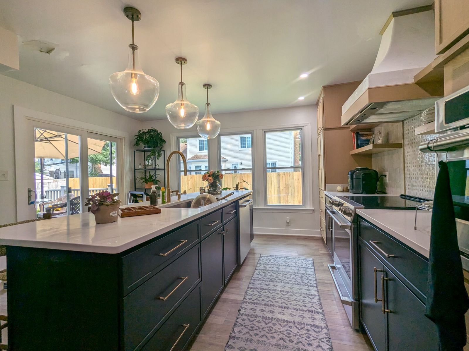 A modern kitchen features dark green cabinets, a white island, three pendant lights, and stainless steel appliances.