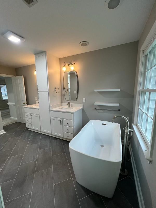 A bathroom with a bathtub , sink , mirror and window.