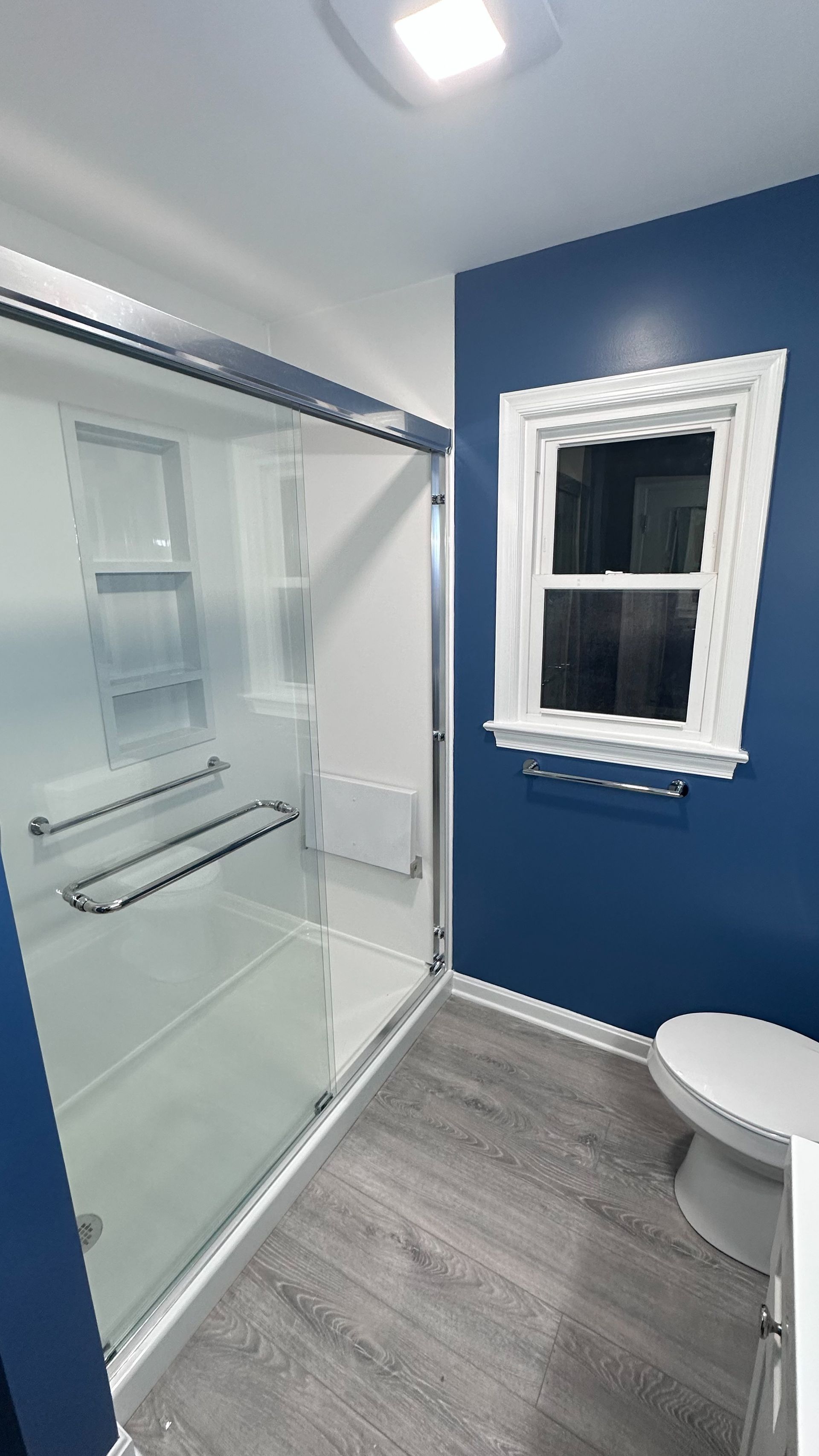 A bathroom with a toilet , shower , and window.