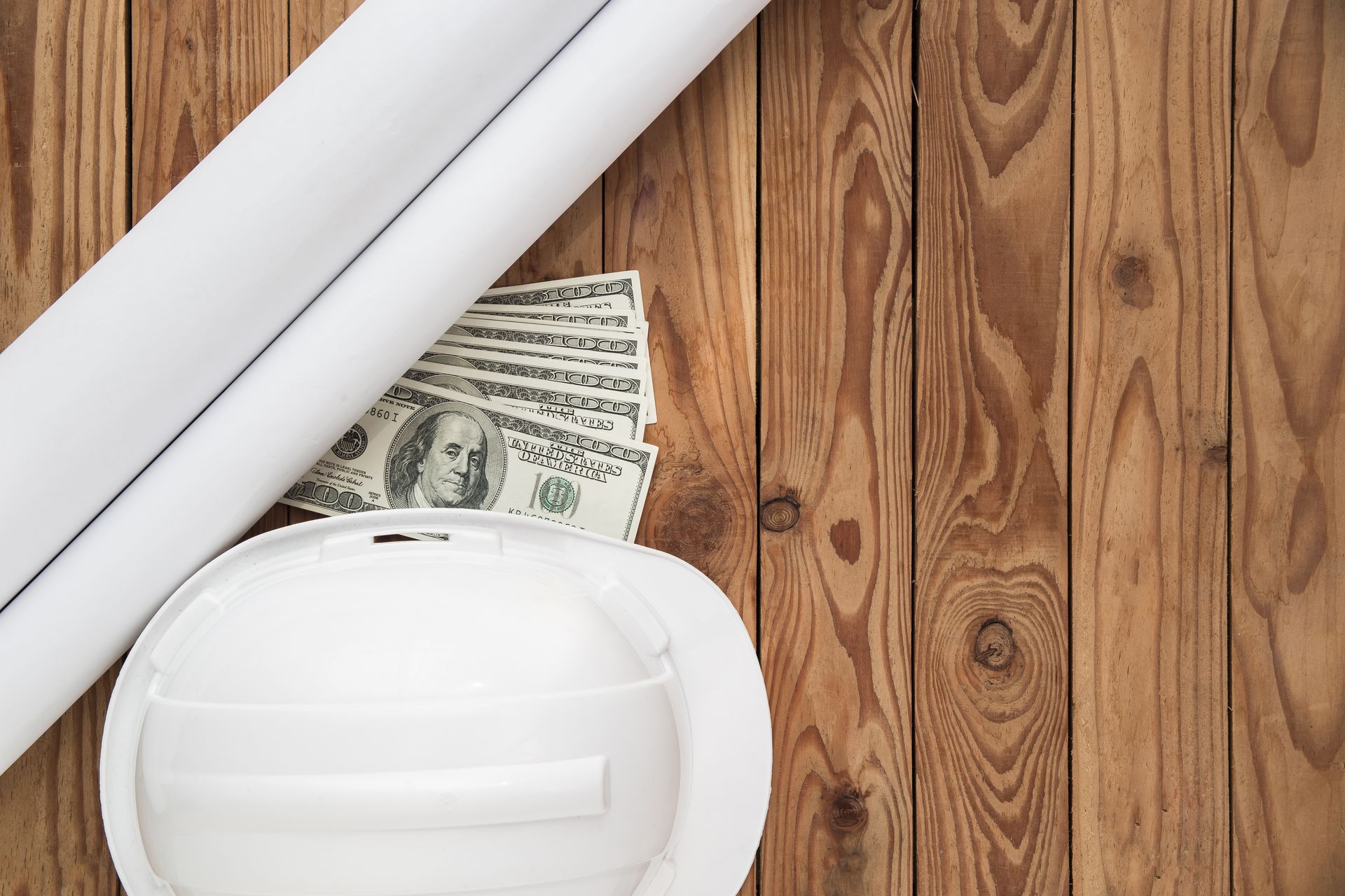 A hard hat , rolls of paper , and money on a wooden table.