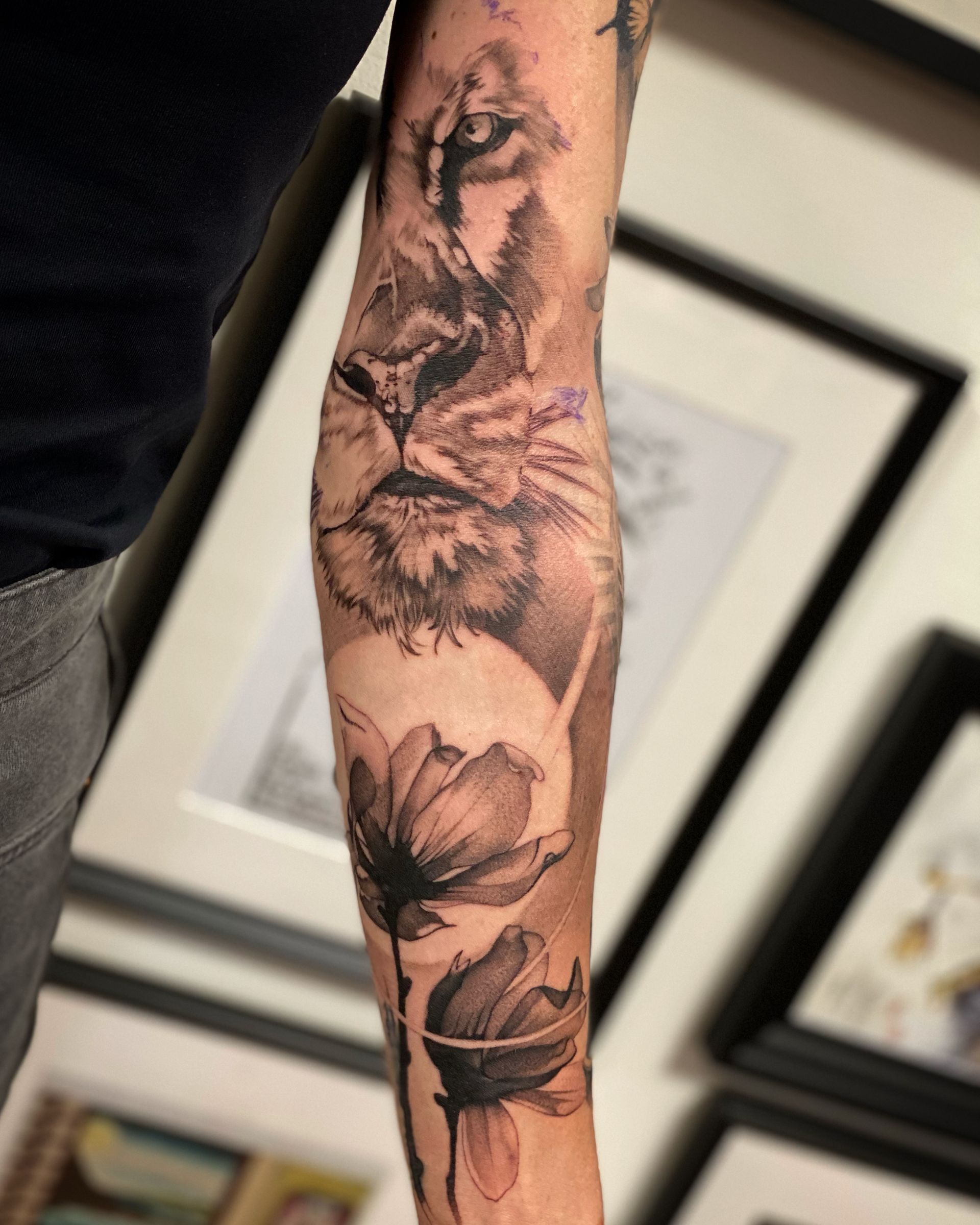Eine Person hat eine Tätowierung mit einem Löwen und Blumen auf dem Arm.