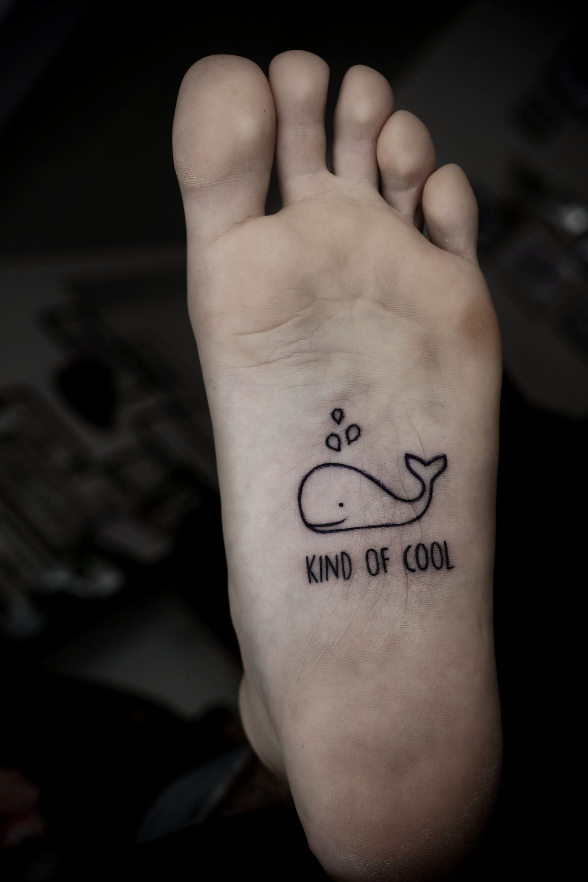 Ein Fuß mit einem Tattoo eines Wals und den Worten „kind cool“
