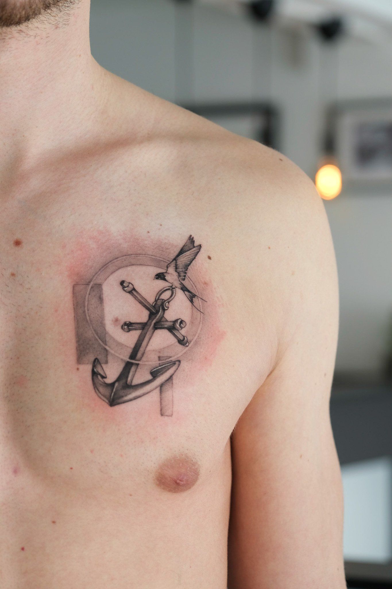 Ein Mann hat ein Tattoo mit einem Anker und einem Kreuz auf seiner Brust.