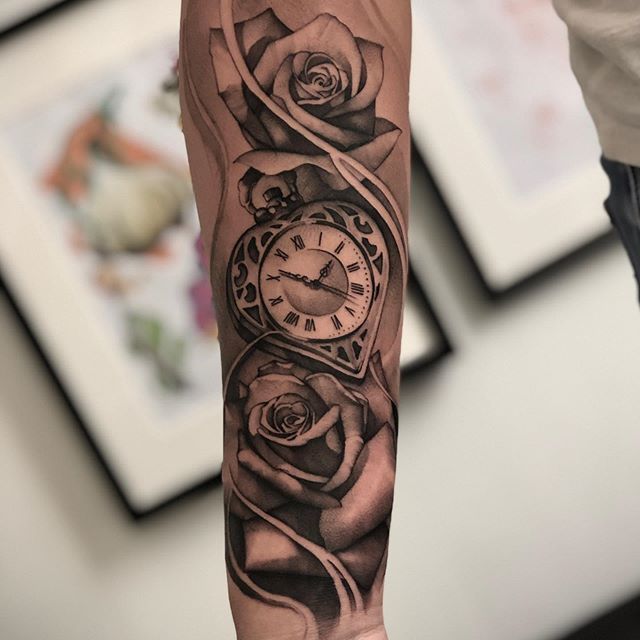 Ein Mann hat eine Tätowierung mit einer Taschenuhr und Rosen auf seinem Unterarm.