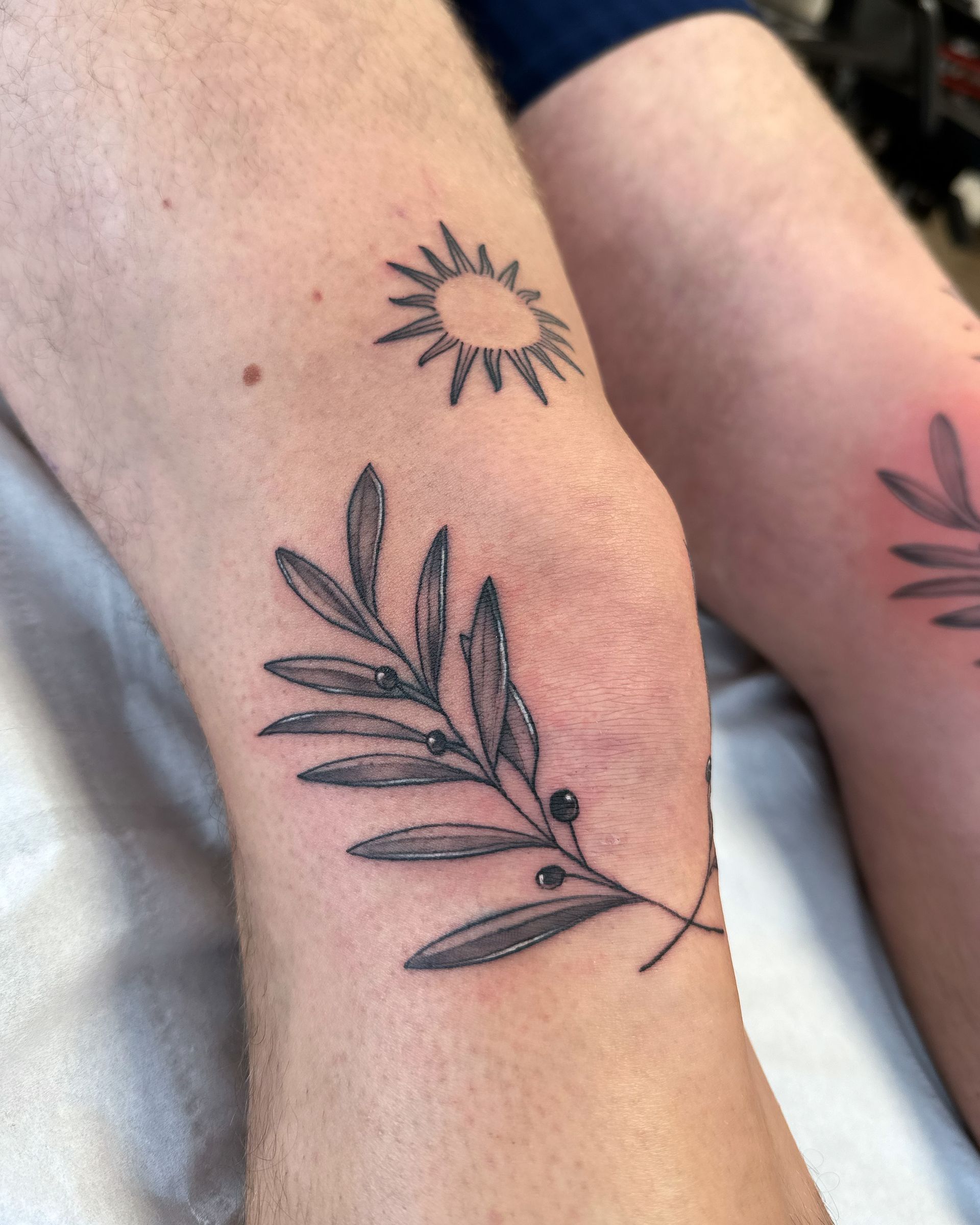 Eine Person hat ein Tattoo mit einem Blatt und einer Sonne auf ihrem Bein