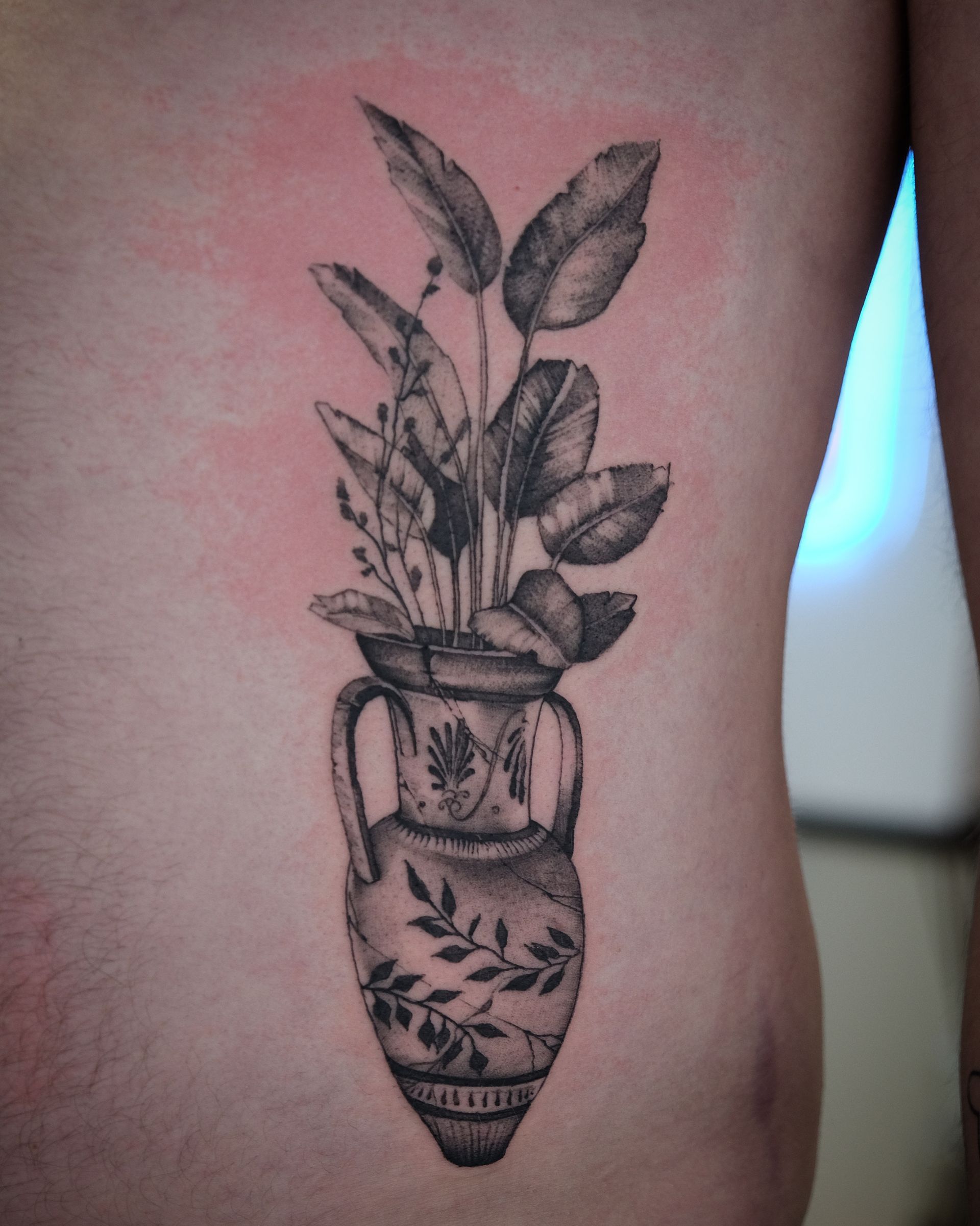 Ein schwarz-weißes Tattoo einer Vase mit Pflanzen darin