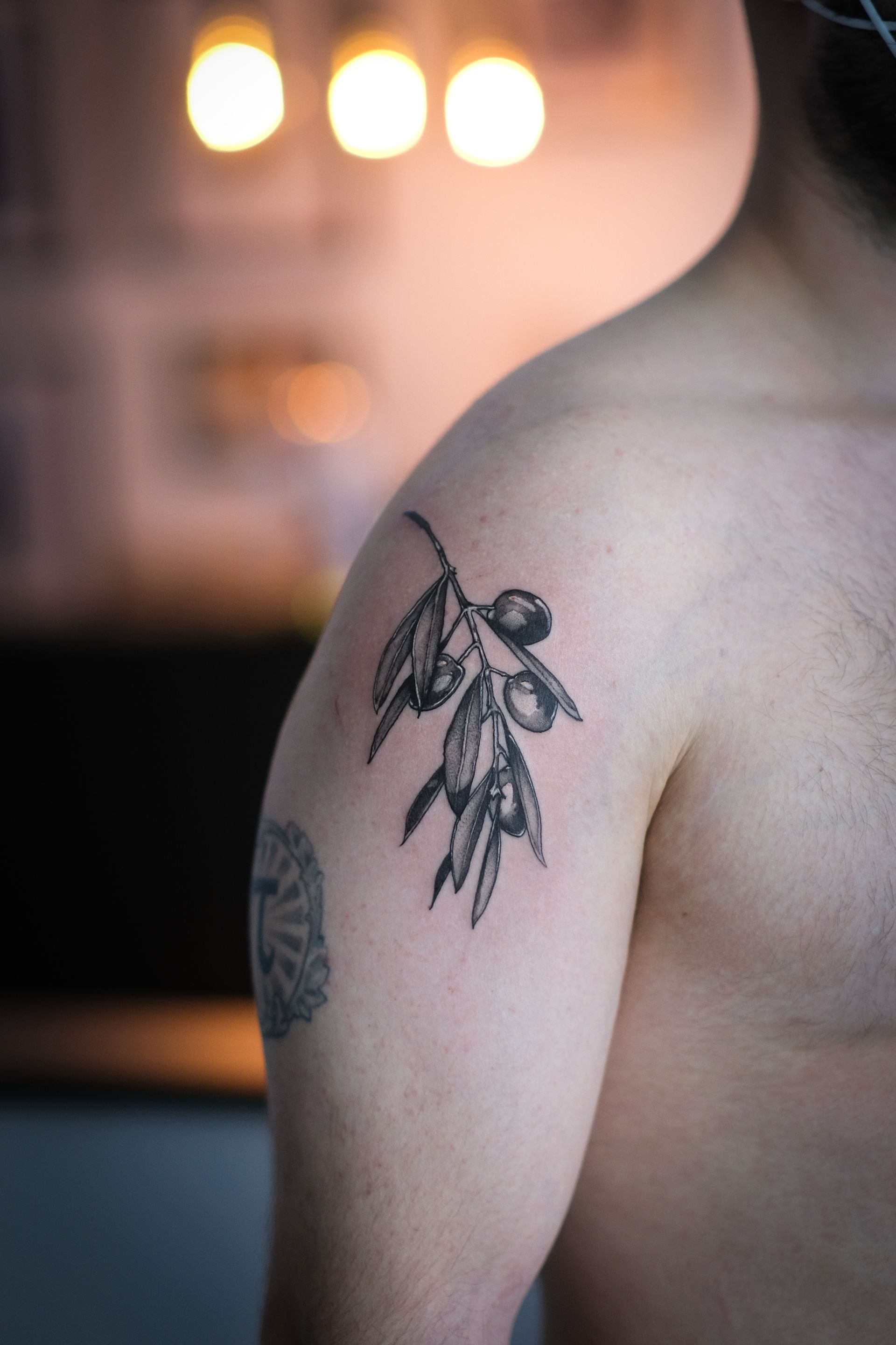 Ein Mann hat ein Tattoo eines Olivenzweigs auf seiner Schulter