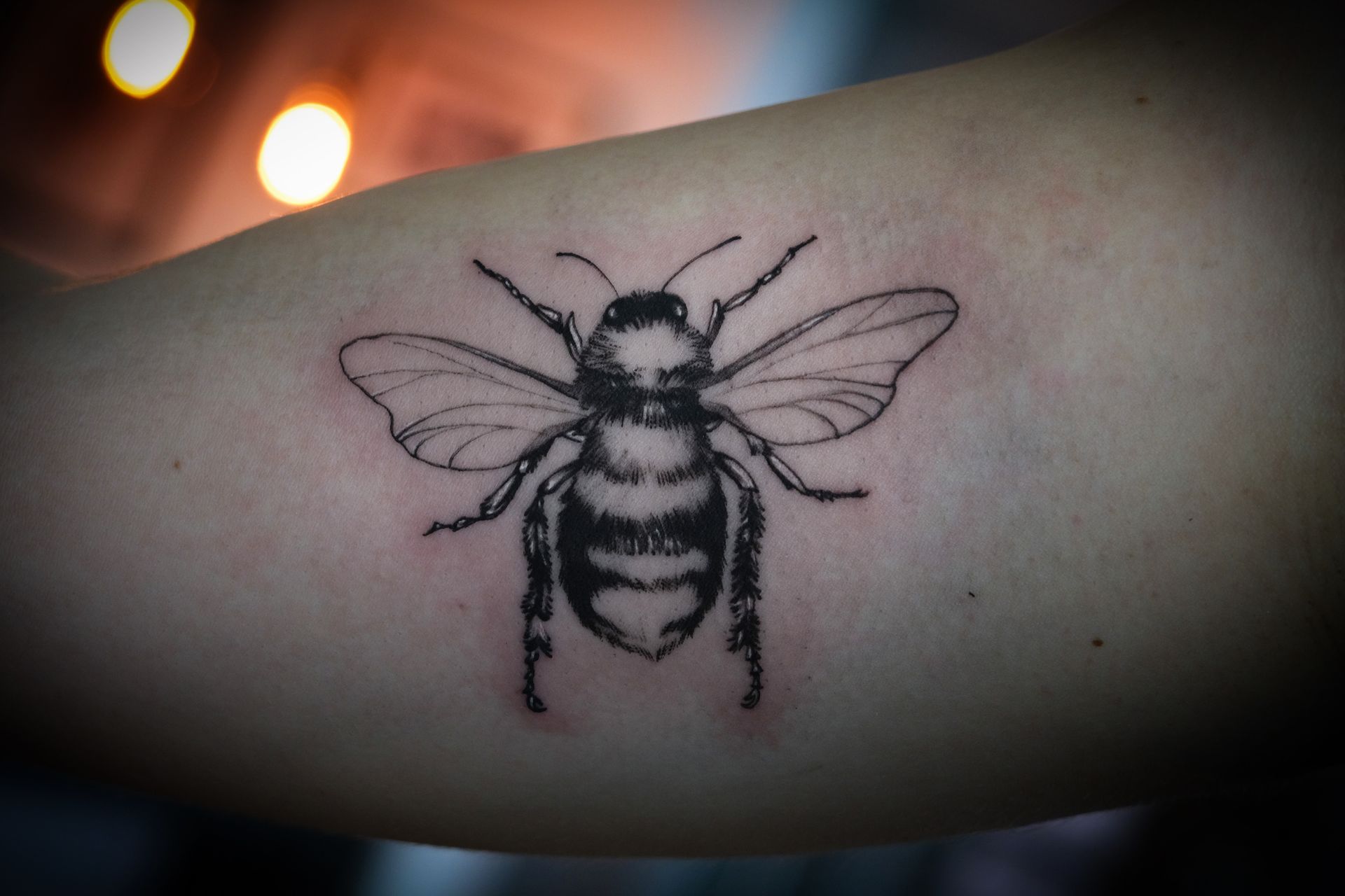 Eine schwarz-weiße Tätowierung einer Biene auf dem Arm einer Person.