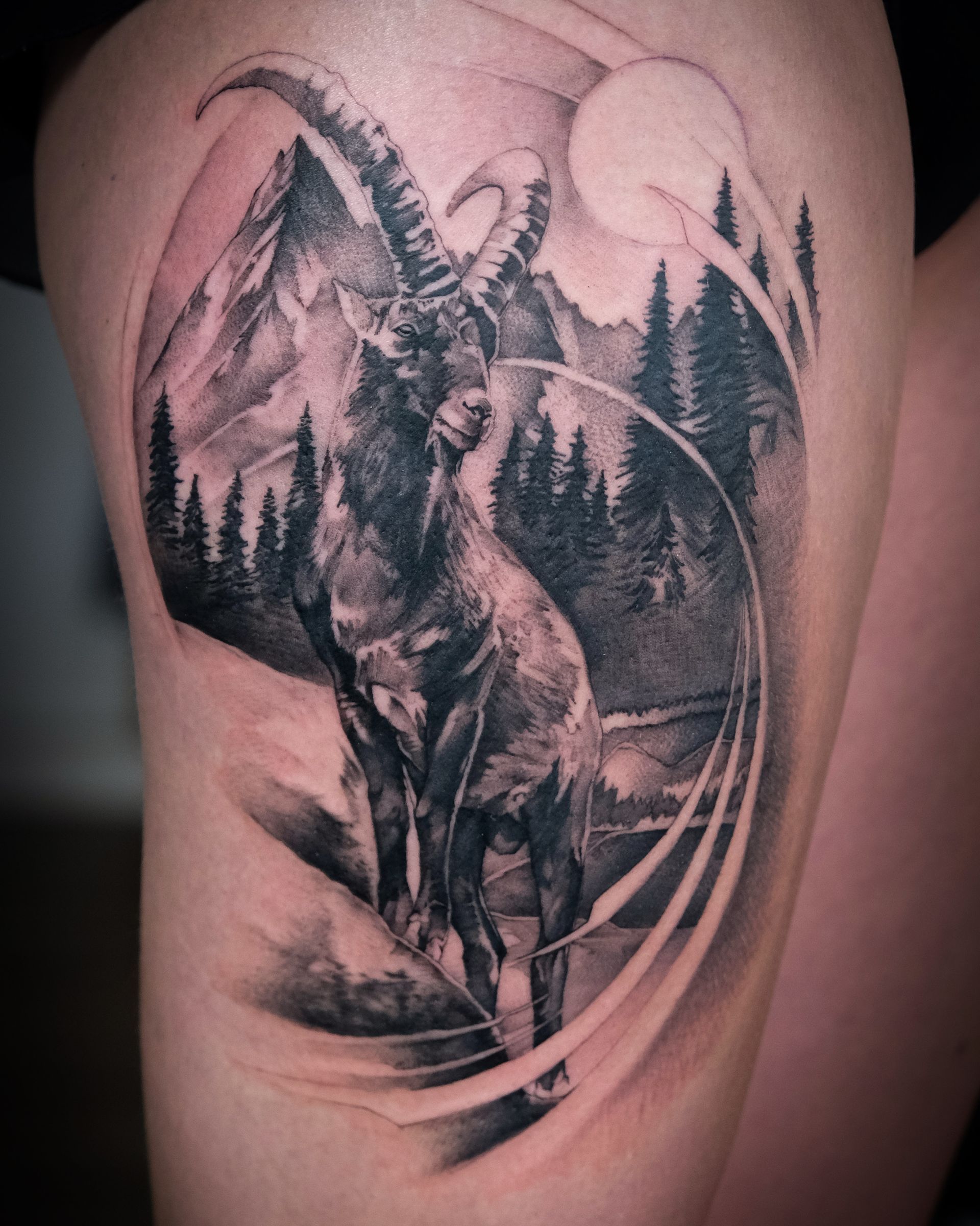 Ein schwarz-weißes Tattoo einer Ziege mit Bergen und Bäumen im Hintergrund