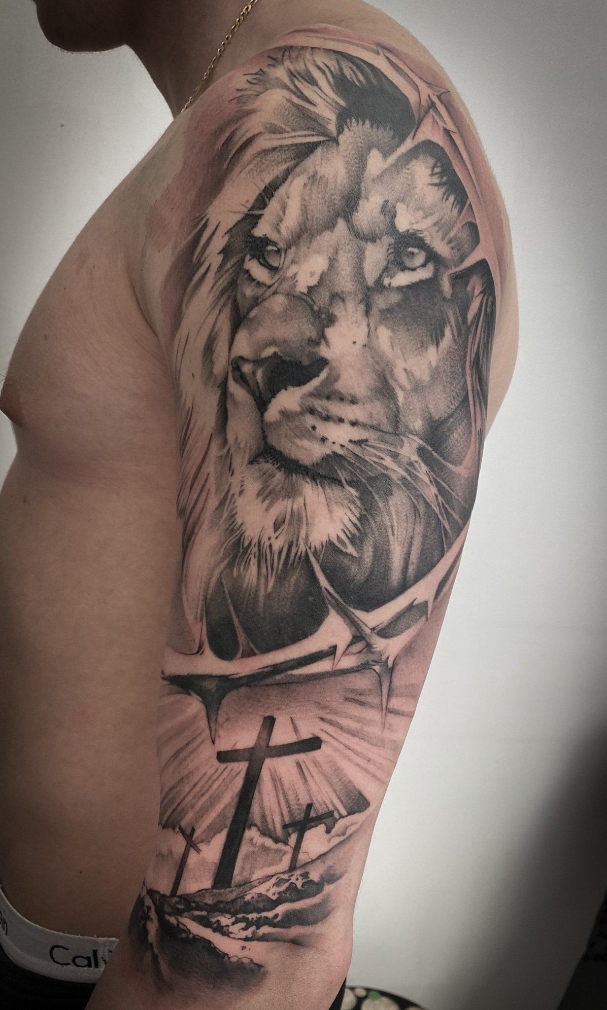 Ein Mann hat eine Tätowierung mit einem Löwen und einem Kreuz auf seinem Arm.