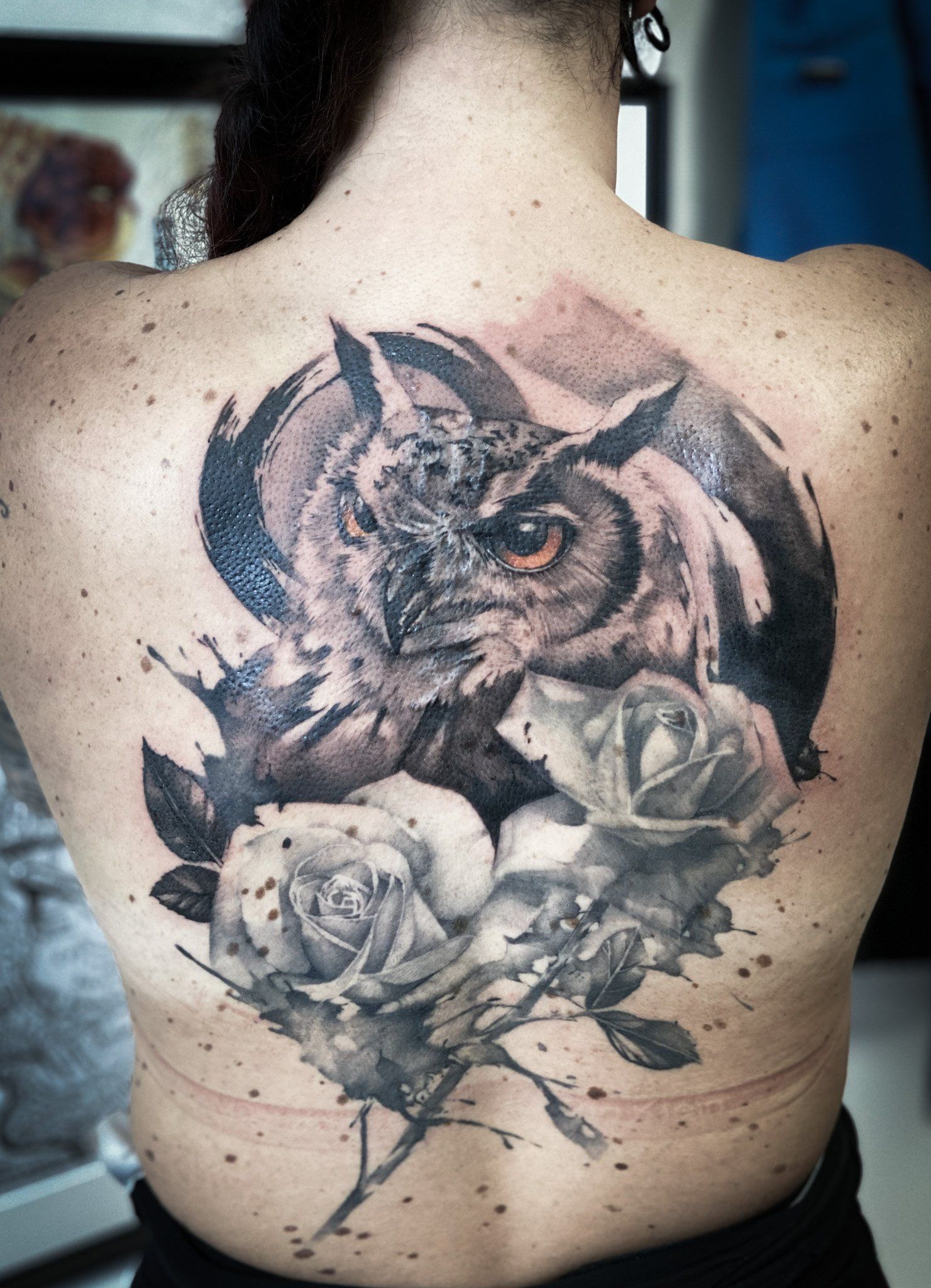 Eine Frau hat eine Tätowierung mit einer Eule und Rosen auf ihrem Rücken.
